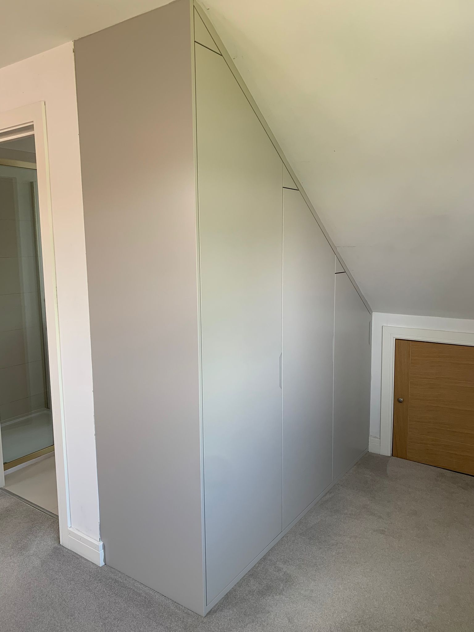 23668 Built-in loft wardrobe with flush handleless doors fitted beneath a sloping ceiling in a Dorset home, featuring bespoke floor-to-ceiling storage with clean modern lines and seamless scribed finish around the roof pitch.