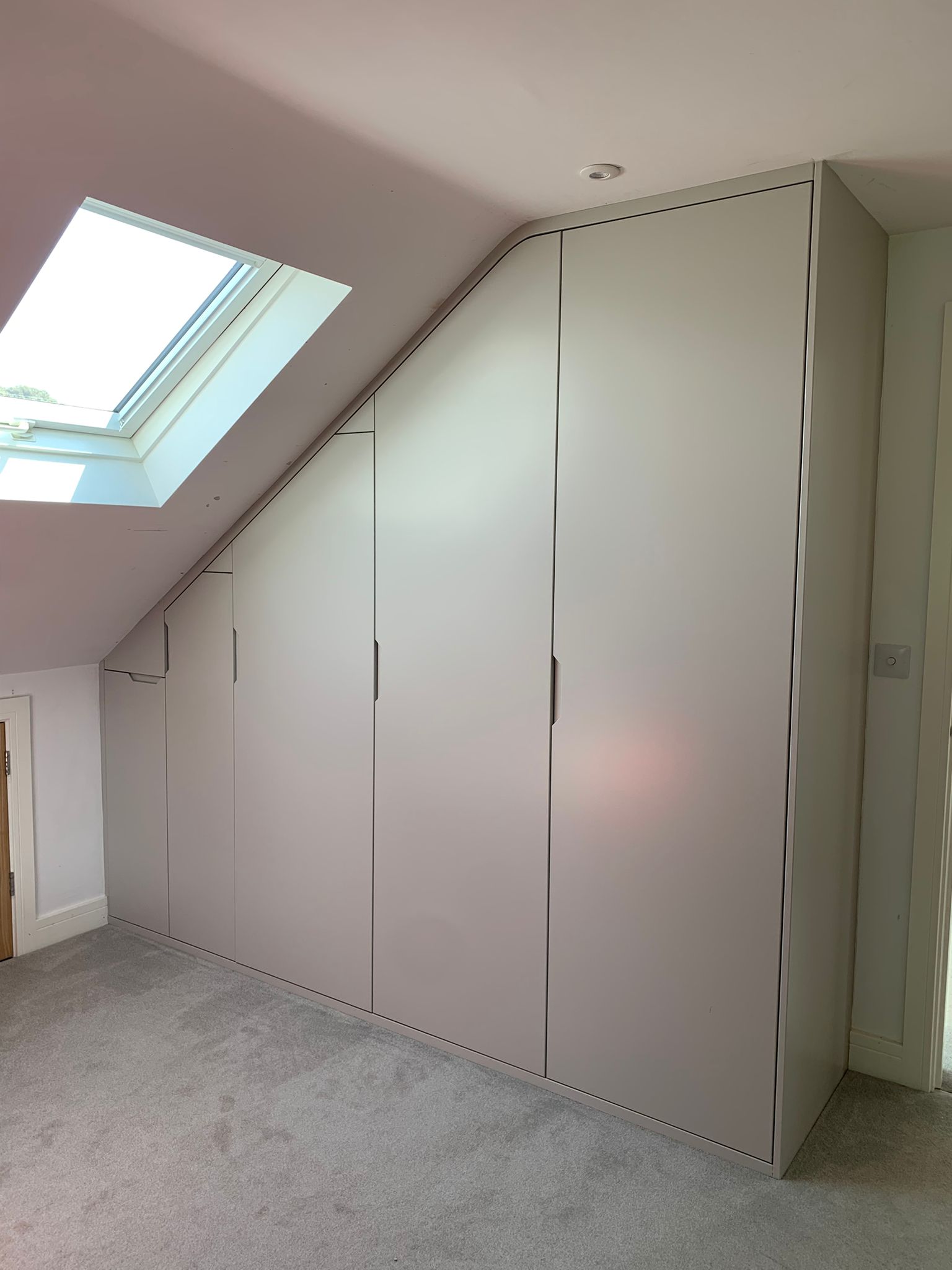 23669 Built-in loft wardrobe with flush handleless doors fitted beneath a sloping ceiling in a Dorset home, featuring bespoke floor-to-ceiling storage with clean modern lines and seamless scribed finish around the roof pitch.