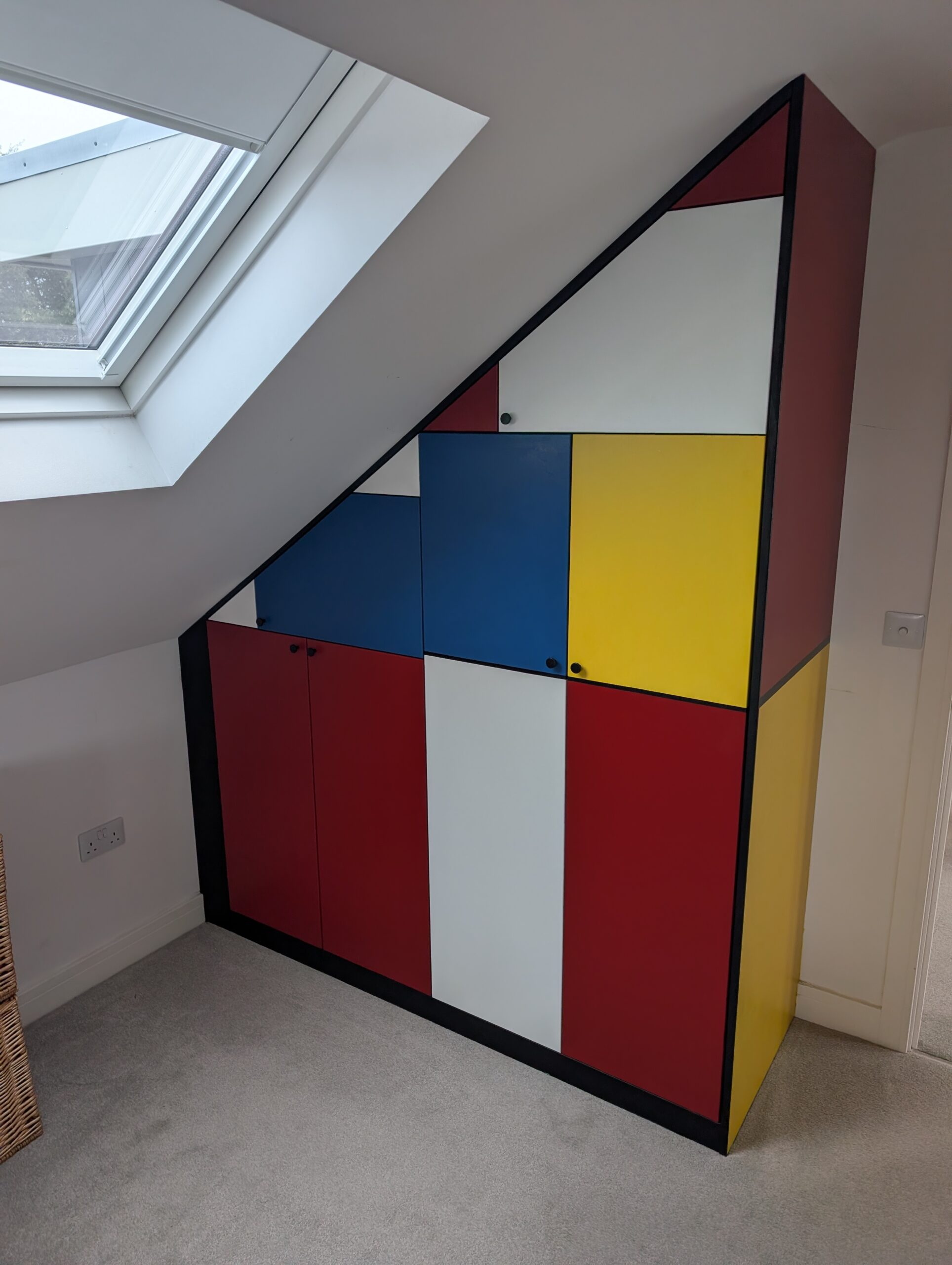 PXL_20251217_104010893 Bespoke under-stairs storage cabinet with sloped ceiling, featuring colourful custom-made doors and fitted shelving, designed and built to fit the space perfectly in Dorset.