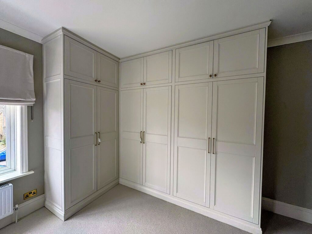 Bespoke fitted shaker wardrobes in painted MDF, built floor-to-ceiling with panelled doors and brass handles, custom made for a bedroom in Dorset